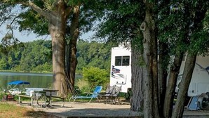 A campsite with a white RV, a picnic table, and blue chairs near a lake. - Lake Blackshear Resort & Golf Club (Cordele)