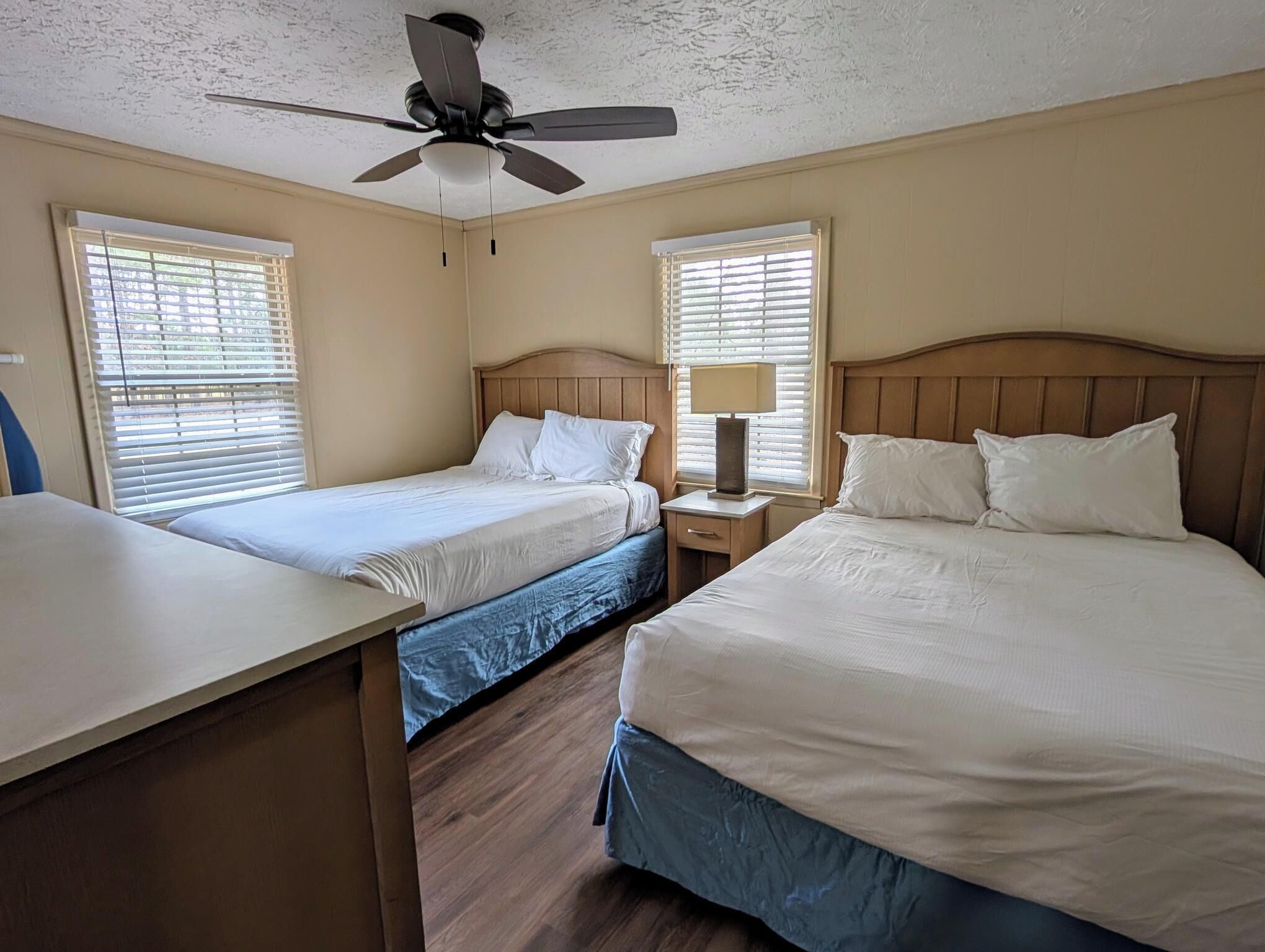A hotel room with two beds, a ceiling fan, and a desk.