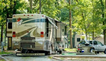 Una vehículo recreativo (RV) con el logo "Winnebago", estacionado en un área boscosa con otra RV y un coche cerca.