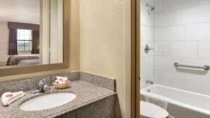 Un baño con lavamanos de encimera de granito, espejo y zona de ducha con bañera.