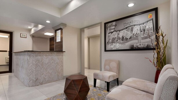 Un área de recepción con un mostrador, una mesita auxiliar de madera hexagonal, dos sillones con cojines, una alfombra estampada y un póster con vista de la ciudad enmarcado en la pared.