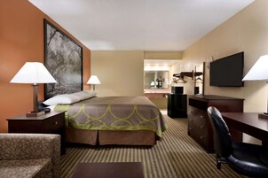 A hotel room with a bed, two bedside lamps, a desk with a chair, a television, a large mirror, and a framed picture on the wall.