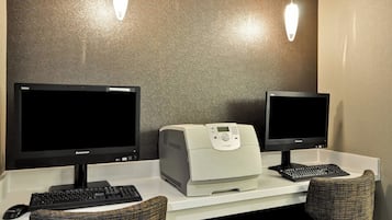 Two monitors, a printer, and a keyboard on a desk with two chairs.