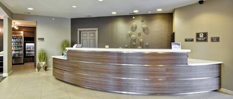 A reception area with a curved reception desk, a wall-mounted display, and a door to the left.