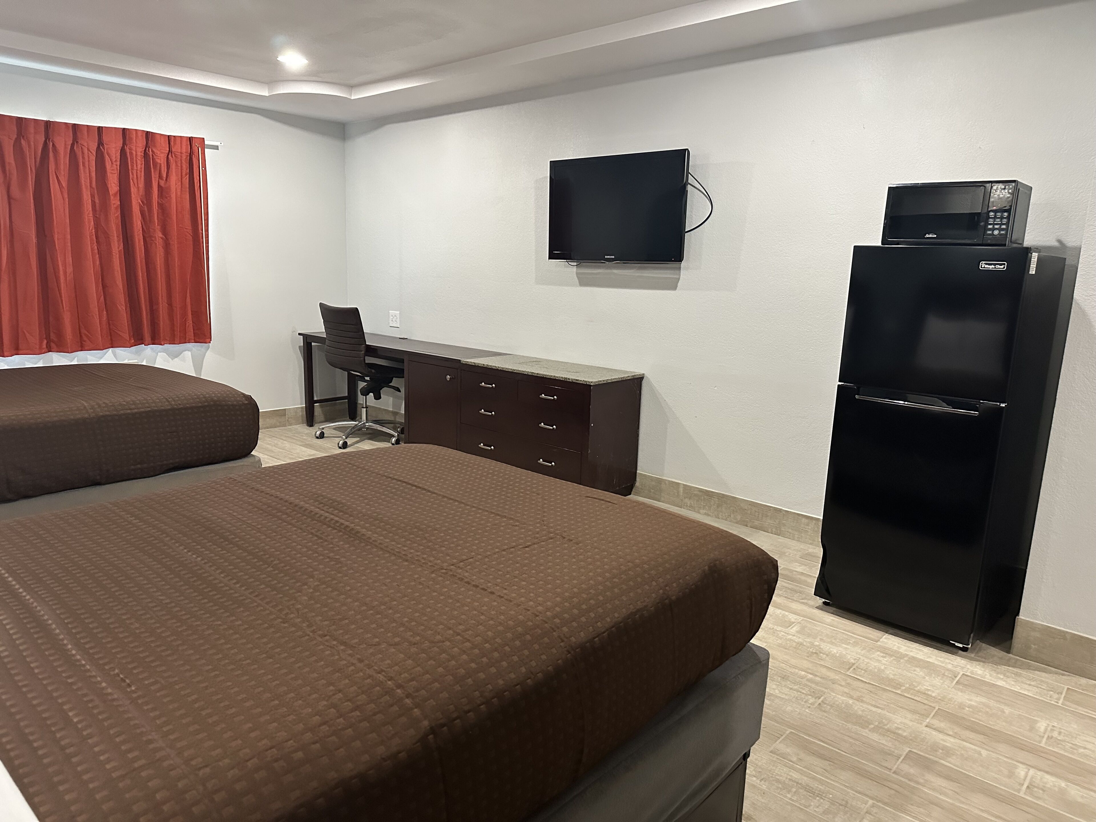 Habitación de hotel con dos camas, un escritorio, una silla, un televisor y un refrigerador.