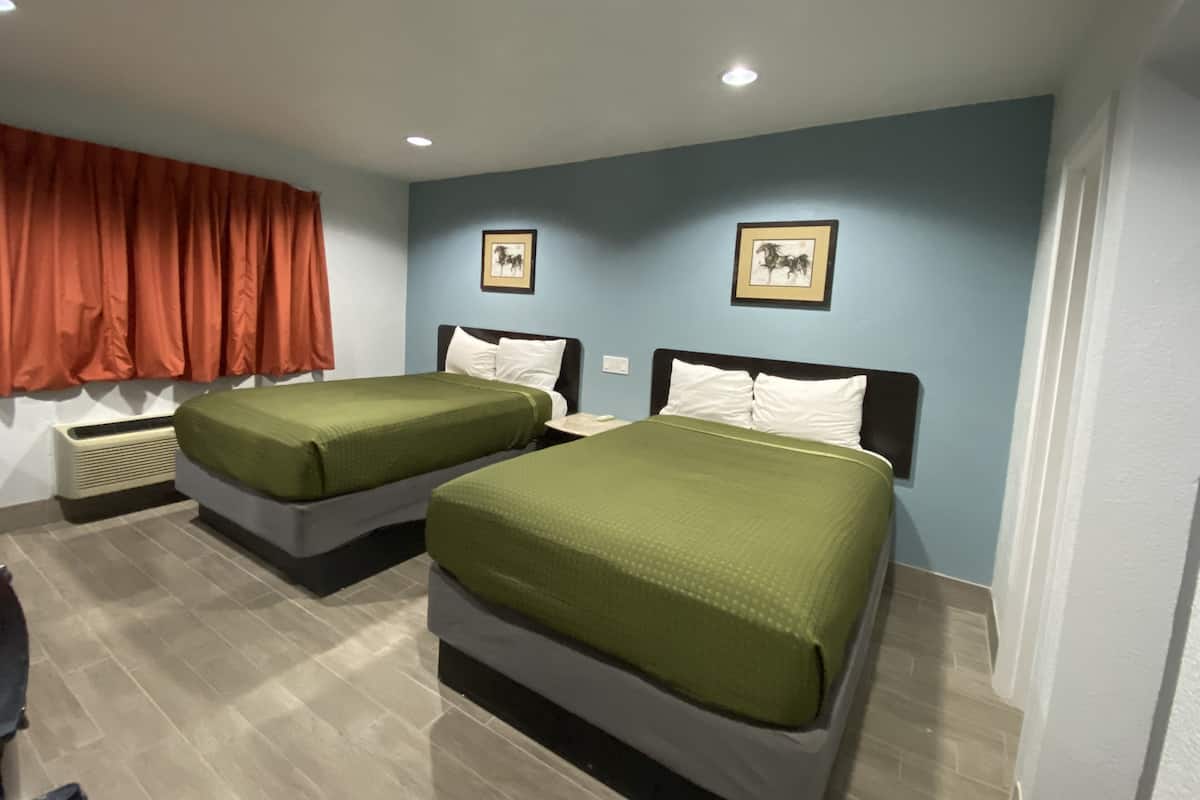Habitación de hotel con dos camas, una cortina roja y dos cuadros en la pared.
