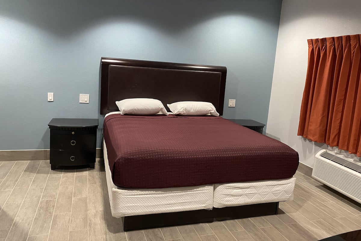 Un dormitorio con una cama grande, dos mesitas de noche, un calentador y una ventana con cortinas.