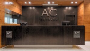 Un comptoir d’accueil orné du logo AC Hotels, un mur revêtu de panneaux en bois et un design moderne.