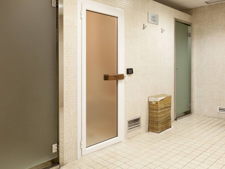 Un baño limpio con azulejos, una puerta color beige y una verde, además de una pequeña cesta de mimbre en el suelo.