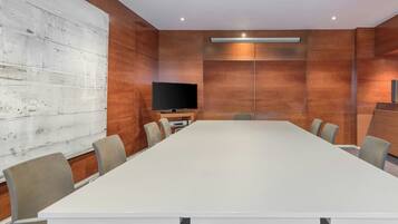 Un salón de conferencias con una larga mesa, sillas, un televisor de pantalla plana y paneles de madera.