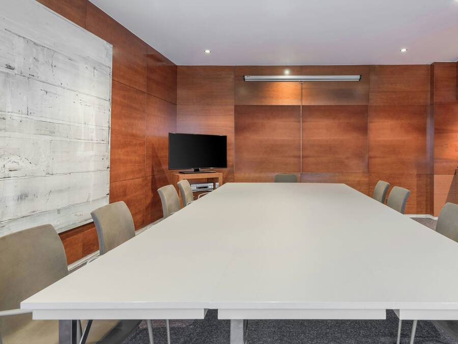 Een vergaderzaal met een lange tafel, stoelen, een flatscreen televisie en houten paneelwanden.