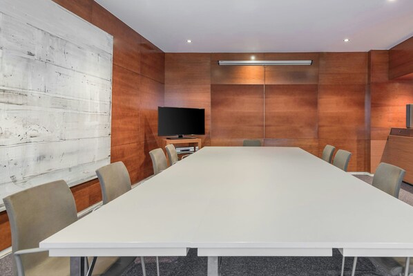 A conference room with a long table, chairs, a flat-screen TV, and wooden panel walls.