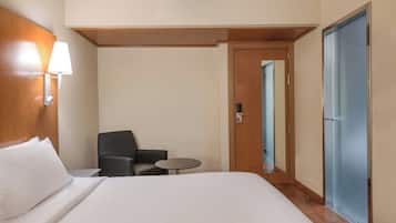 Een hotelkamer met een bed, een stoel, een klein tafeltje, een lamp en een deur.