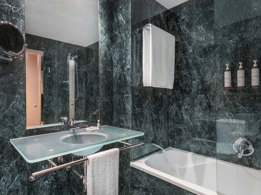 Un baño moderno con lavamanos de vidrio, bañera y paredes de mármol.