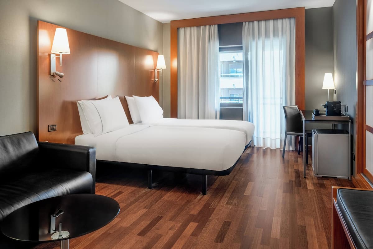 A hotel room with a large bed, a desk, a chair, and a small table.