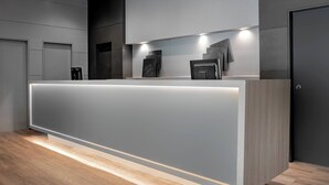 A modern reception desk with a lighted base, a dark wall, and a wooden floor. - AC Hotel Ponferrada by Marriott (Ponferrada)