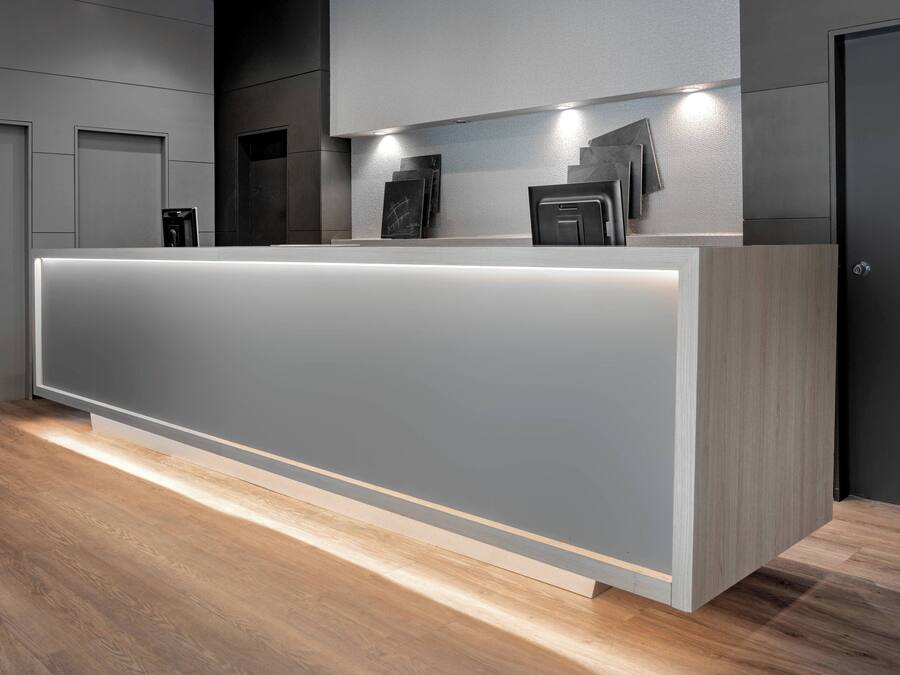 A modern reception desk with a lighted base, a dark wall, and a wooden floor.