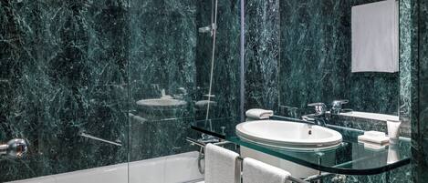 Un baño moderno con ducha de vidrio, una bañera blanca y un lavamanos de vidrio.