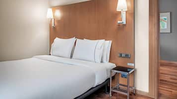 A hotel room with a large bed, two wall-mounted lamps, a small bedside table, and a wooden headboard.