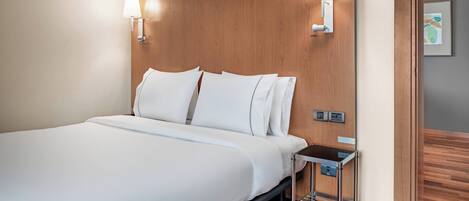 Une chambre d’hôtel avec un grand lit, deux lampes fixées au mur, une petite table de chevet et une tête de lit en bois.