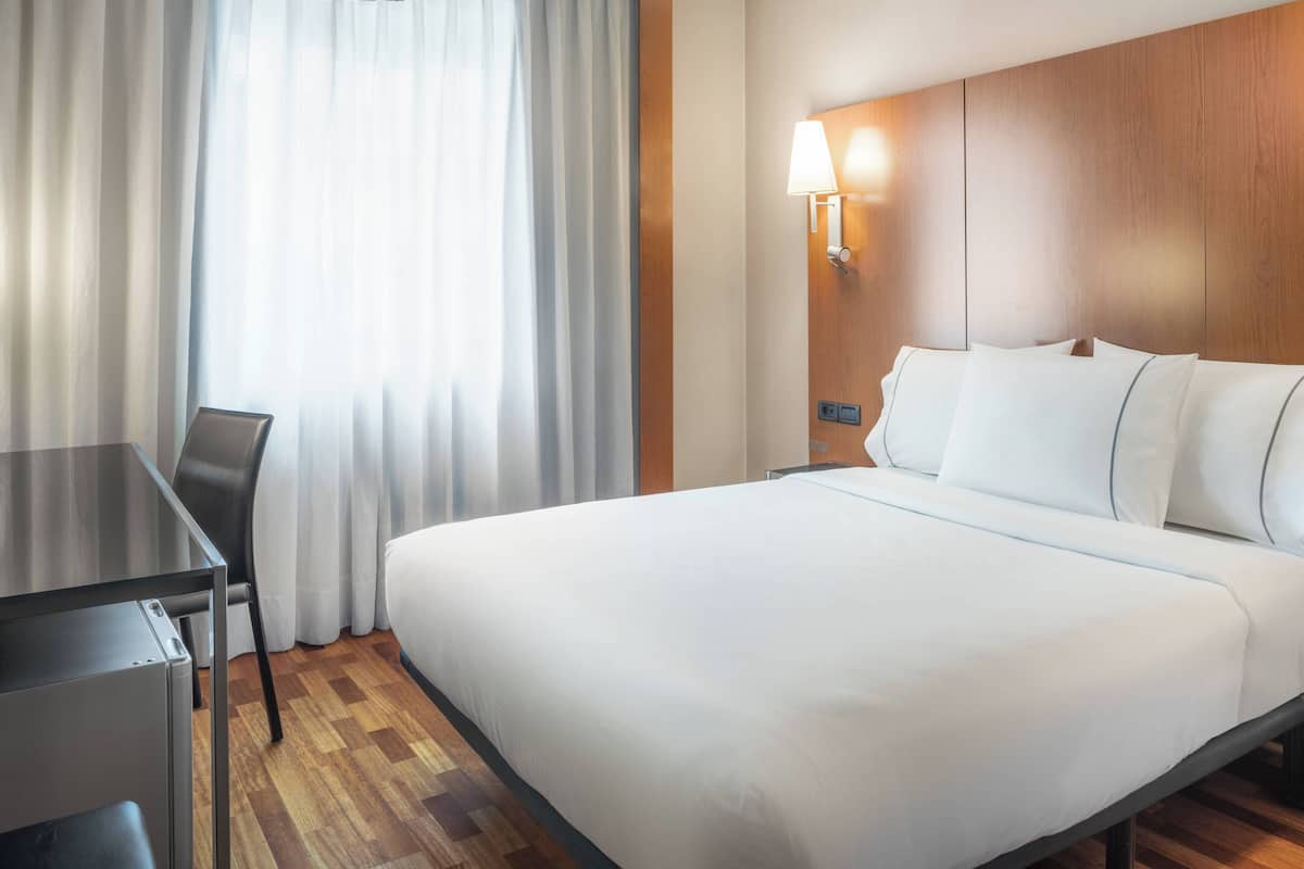 A hotel room with a bed, a desk, and a lamp.