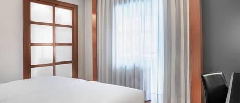 Una habitación de hotel con una cama, una ventana con cortinas, una puerta de madera y una silla.