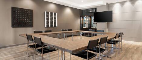 Een vergaderruimte met een lange tafel, stoelen, een flatscreen televisie en wanddecoratie.