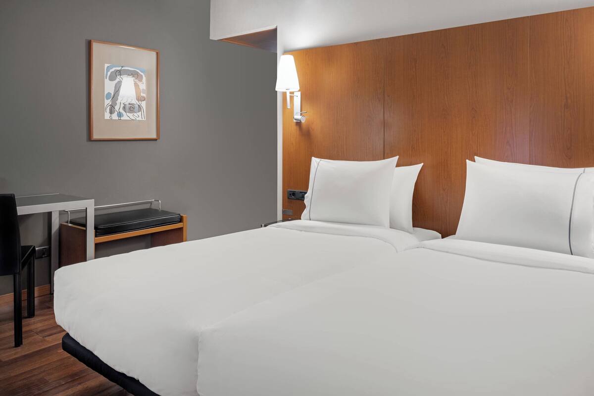 A hotel room with a large bed, a desk, a chair, and a framed picture on the wall.
