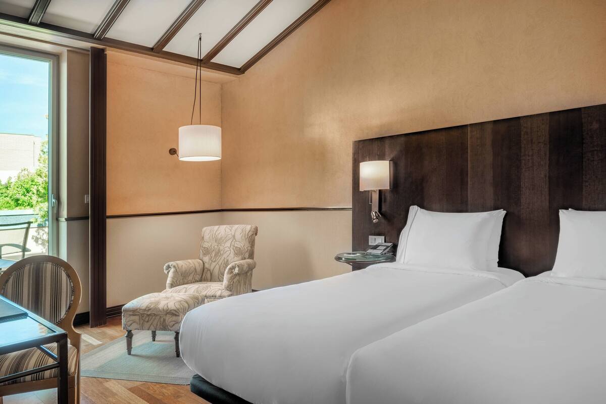Quarto de hotel com uma cama grande, uma cadeira, uma mesa e vista para o exterior.