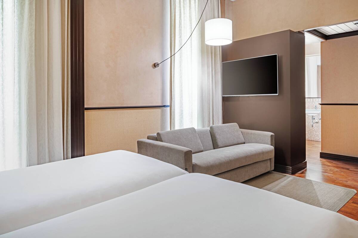 Quarto de hotel com uma cama grande, um sofá, uma televisão de tela plana na parede e um lustre.