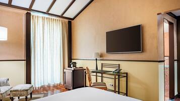 Habitació d'hotel amb un llit, una escriptori amb una làmpada, una cadira, un televisor fixat a la paret i una finestra amb cortines.