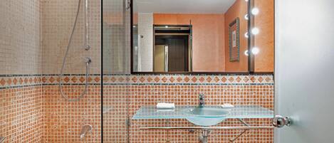 A bathroom with a glass shower enclosure, a glass sink, and a bathtub.