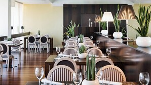 A well-lit dining area with multiple tables set for service, featuring striped chairs and potted plants. - AC Hotel Ciudad de Tudela by Marriott (Tudela)
