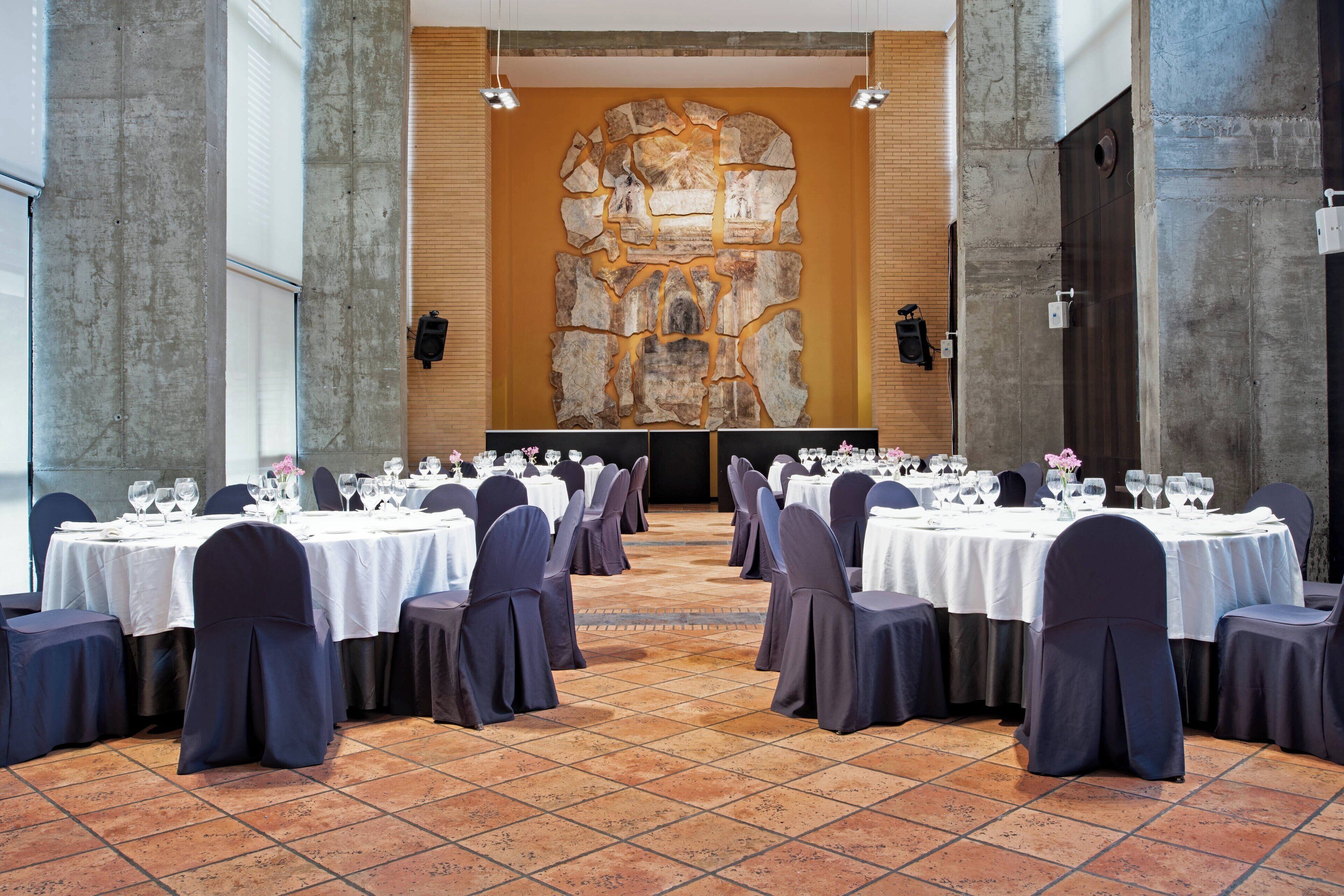 Une salle de banquet avec de nombreuses tables rondes disposées pour le repas, chacune étant agrémentée de chaises et de couverts.