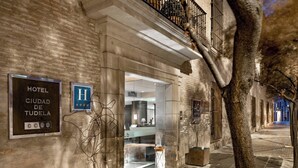 A hotel entrance with a sign reading "HOTEL CIUDAD DE TUDELA," a glass door, and a tree in the foreground. - AC Hotel Ciudad de Tudela by Marriott (Tudela)