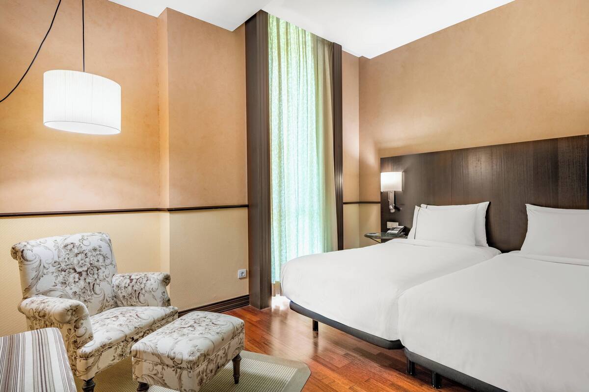 Quarto de hotel com uma cama grande, uma cadeira, uma mesa pequena e um abajur.