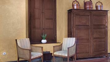 Een kamer met twee rieten stoelen, een houten kast met koperen emmers en een plant in een pot op een vensterbank.