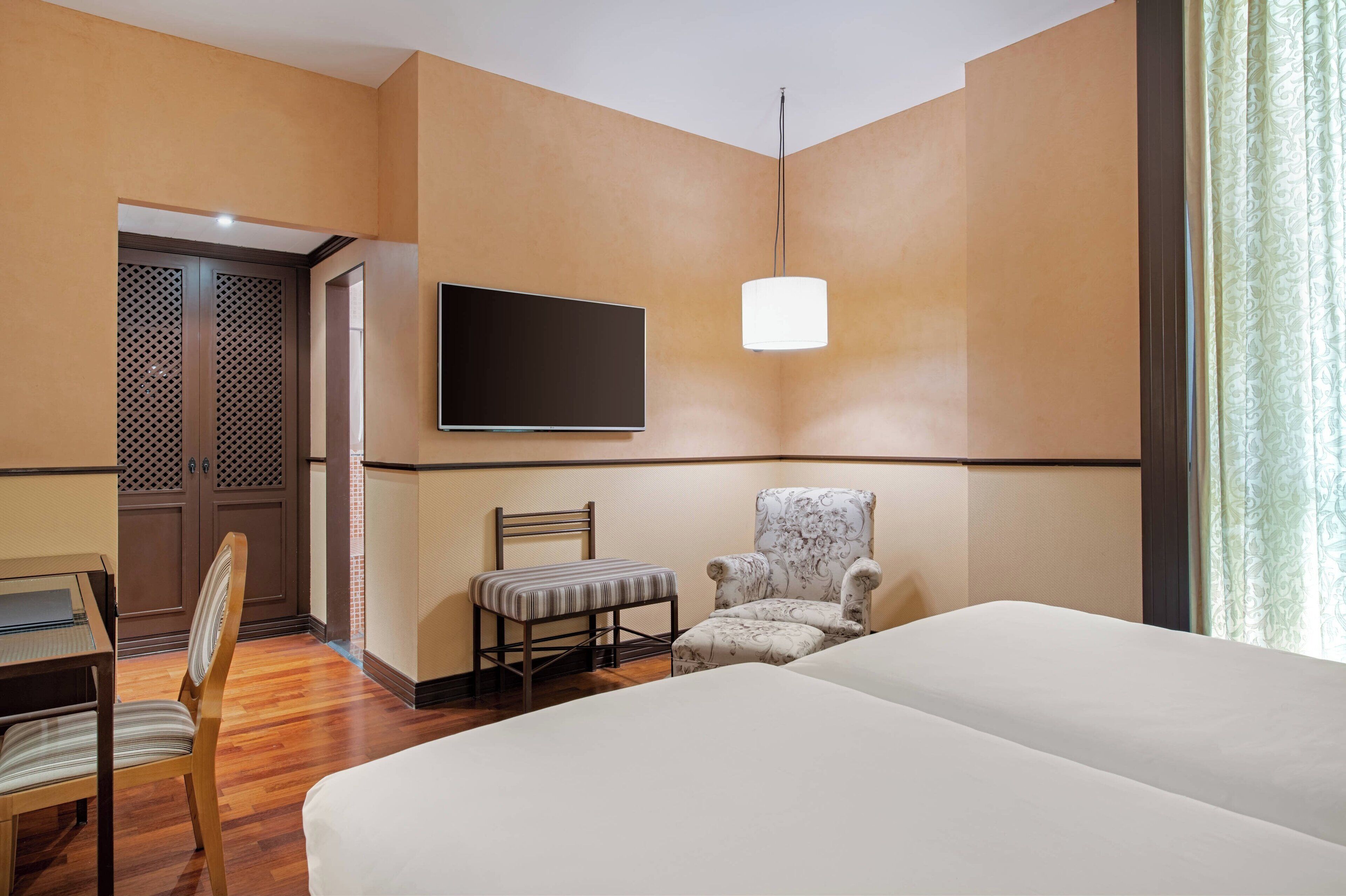 Een hotelkamer met een bed, een bureau, een stoel, een televisie en een gestreept fauteuil.