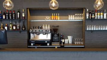 A bar area with shelves of liquor bottles, a coffee machine, and hanging light fixtures.