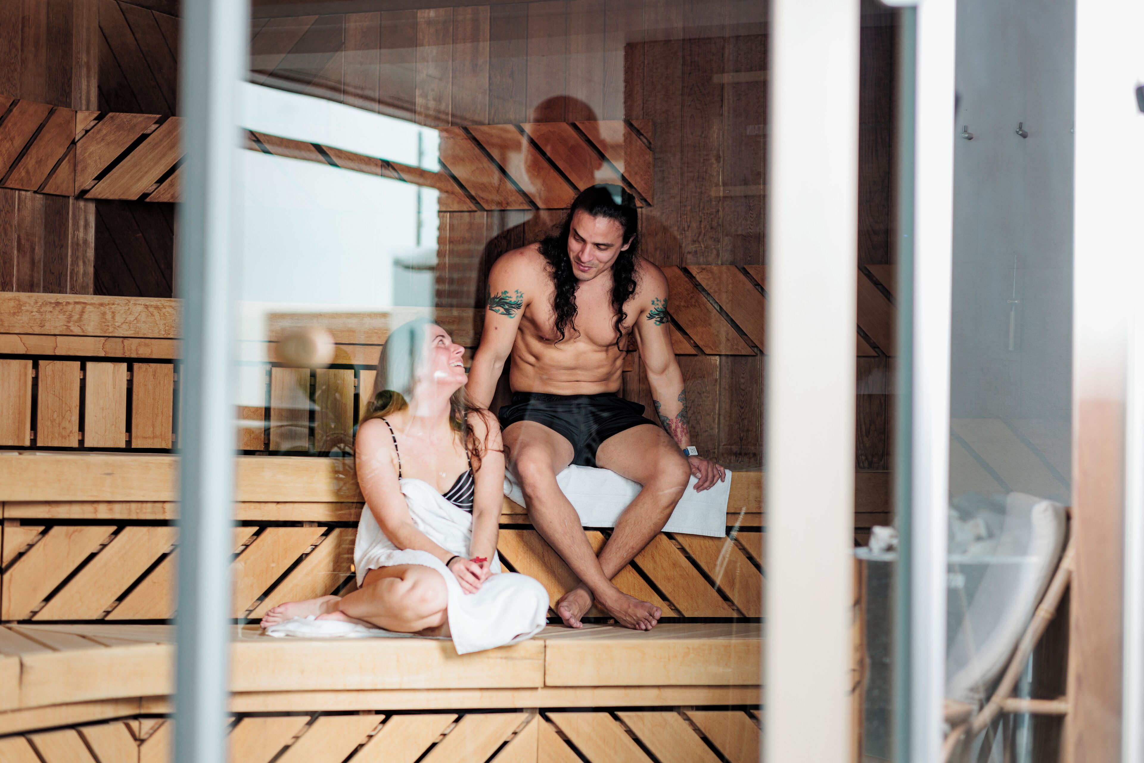 A wooden bench with a glass partition, a person sitting on the bench, and another person standing beside them.