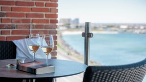 A table with two wine glasses and a book, a brick wall, and a view of a body of water. - Griffen Spahotel (Ronne)