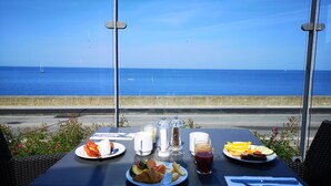 A table with breakfast items and a glass of juice, overlooking a coastal road with a view of the sea. - Griffen Spahotel (Ronne)