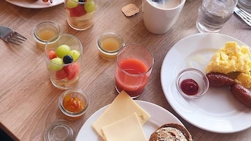 A breakfast table with various food items and drinks, including toast, eggs, sausages, cheese, and fruit.