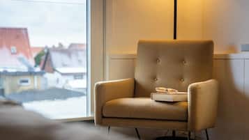 Una silla con un libro, gafas, una lámpara y vistas de edificios a través de una ventana.
