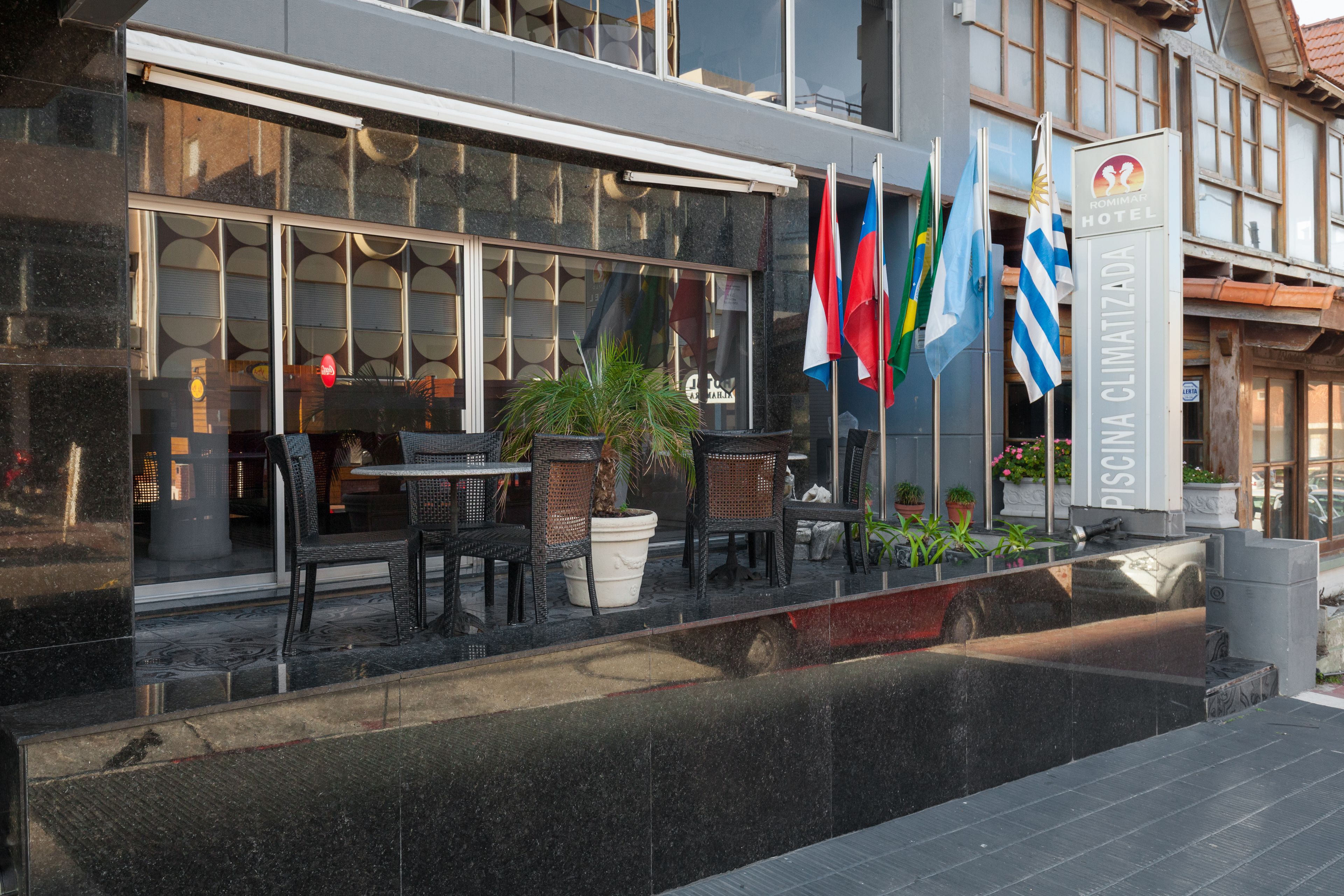 A hotel exterior with outdoor seating, flags, and a sign indicating the name 'Rimini Hotel'.