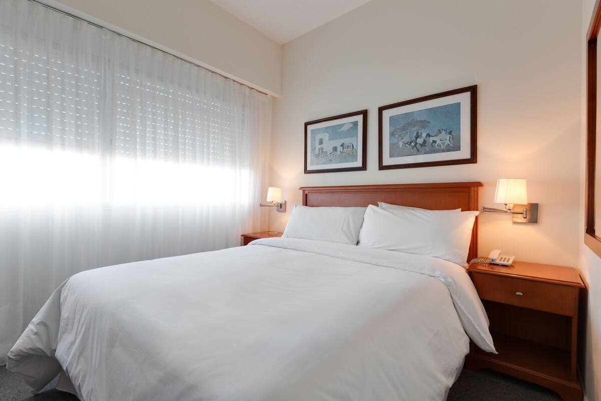 A hotel room with a large bed, two bedside tables with lamps, and two framed pictures on the wall.