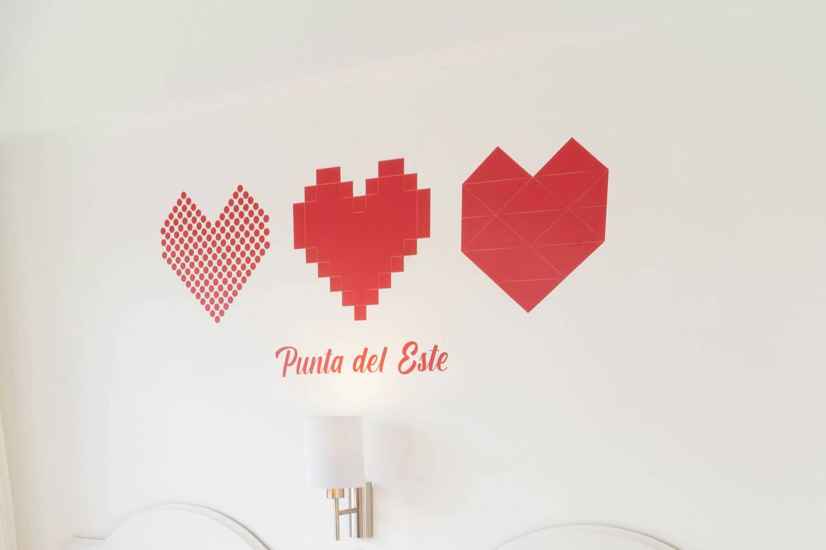 A hotel room with two beds, a bedside table with a phone, and a wall with three heart-shaped decorations.