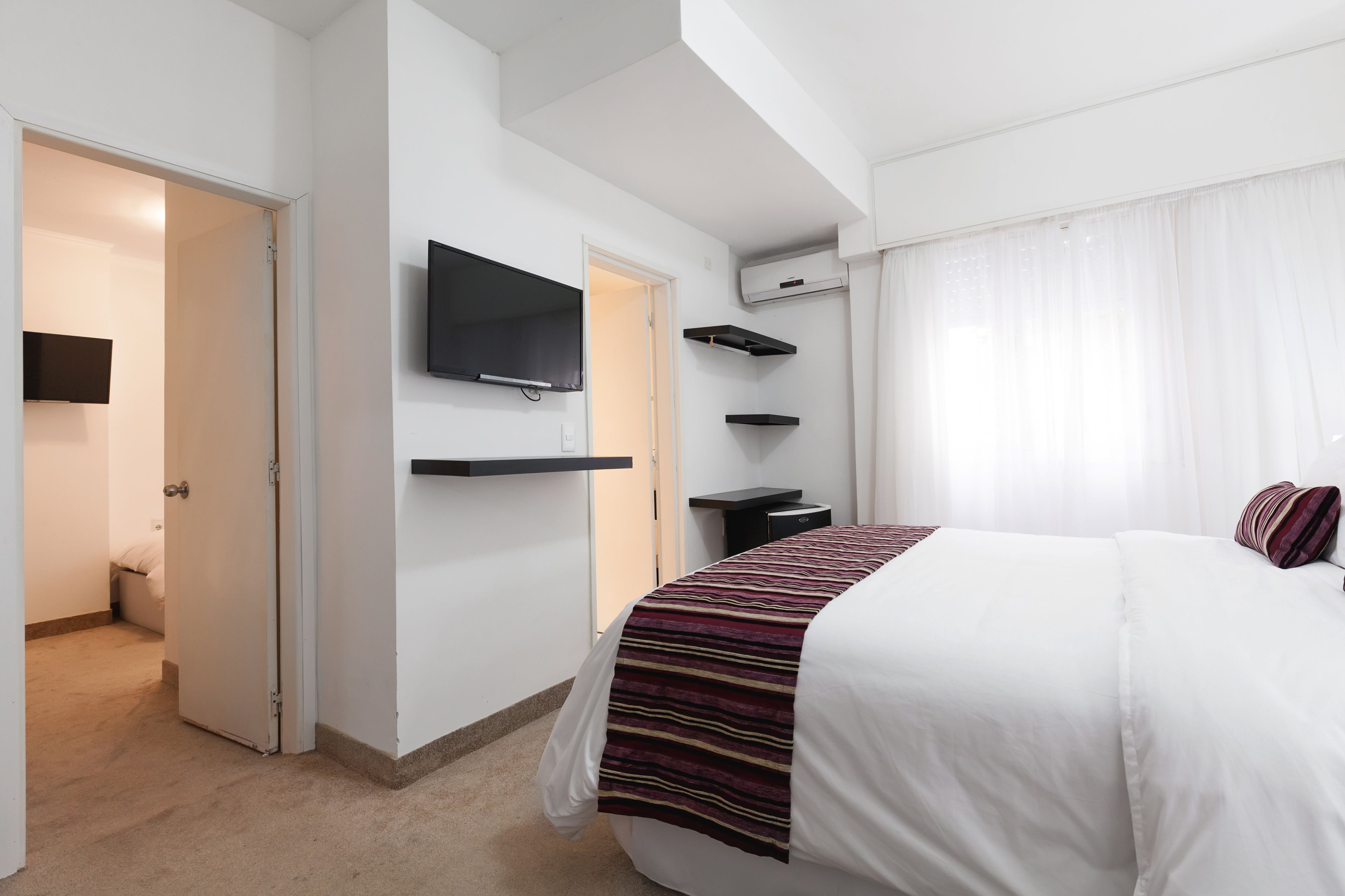 A modern hotel room with a large bed, a flat-screen TV mounted on the wall, and built-in shelves.