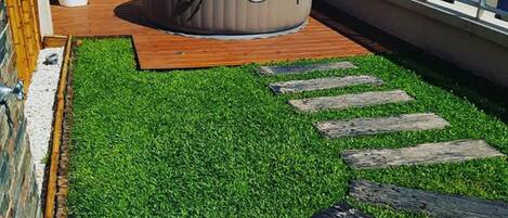 Una terraza en la azotea con césped artificial, un jacuzzi y vista al océano.