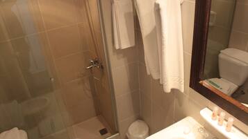 A bathroom with a glass shower enclosure, a toilet, a sink with toiletries, and a mirror.